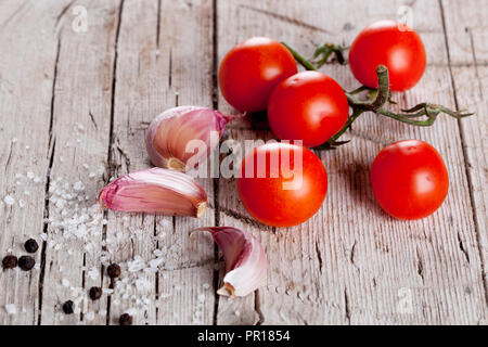 Pomodori ciliegini, aglio, pepe e sale in stile rustico sfondo di legno Foto Stock