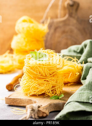 Pasta all'uovo fatta a mano le tagliatelle nido sul tagliere di legno con foglia di basilico. Un sano cibo italiano concetto. Foto Stock