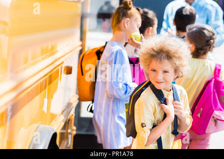 Felice parentesi scolaro con i compagni di classe in piedi vicino a scuola bus Foto Stock