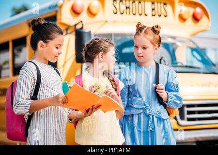 Gruppo di adorabili poco studentesse con i notebook parlando nella parte anteriore del bus di scuola Foto Stock