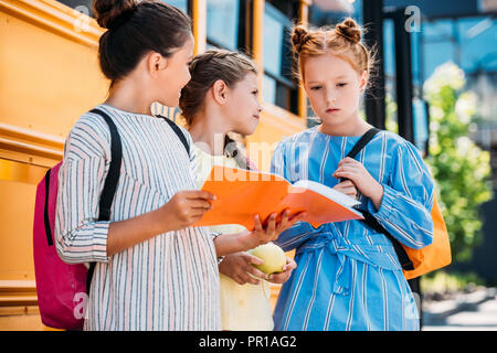 Un gruppo di studentesse poco con i notebook parlando nella parte anteriore del bus di scuola Foto Stock