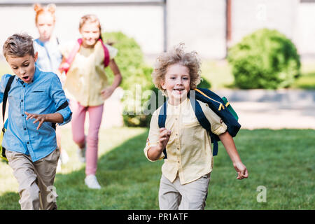 Felice scolaro con i compagni di classe che corrono dal giardino della scuola Foto Stock