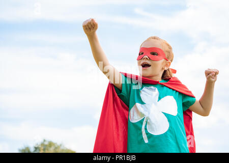 Adorabili bambini in costume da supereroe con braccio teso e il blu cielo nuvoloso sullo sfondo Foto Stock