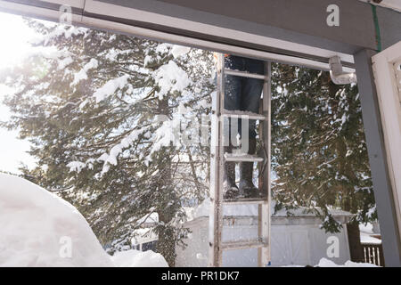 Uomo di neve di pulizia dal tetto del suo negozio Foto Stock