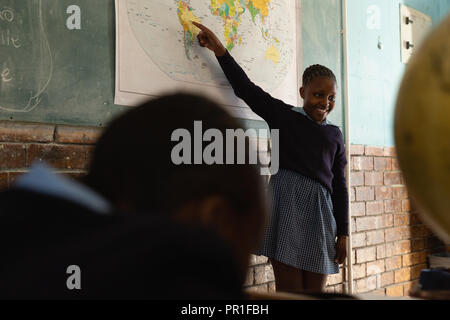 Schoolgirl spiegando sulla mappa del mondo in classe Foto Stock