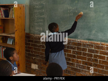 Schoolgirl scrivere sulla lavagna in aula Foto Stock