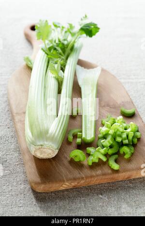 Testa di sedano su un tagliere di legno con fettine di sedano che giace accanto ad essa. Foto Stock