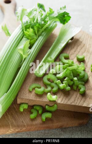 Testa di sedano su un tagliere di legno con fettine di sedano che giace accanto ad essa. Foto Stock