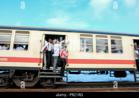 Sri Lanka uomini d'affari che cavalcano a porta aperta del treno pendolari a Colombo, Sri Lanka Foto Stock