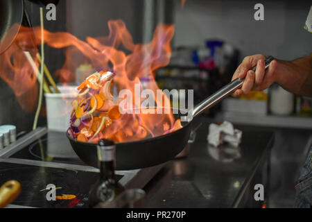 Lo Chef tossing flambe verdure in una padella il bruciatore Foto Stock