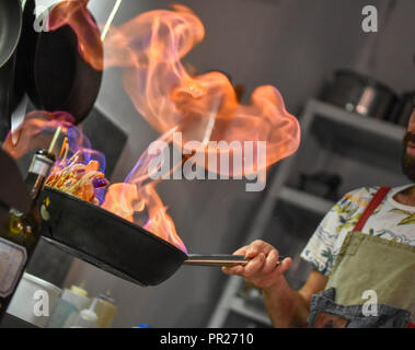 Lo Chef tossing flambe verdure in una padella il bruciatore Foto Stock