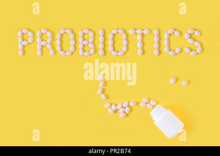 Probiotici parola fatta di pillole su sfondo giallo. Appartamento laico, vista dall'alto, copia gratuita dello spazio. Foto Stock
