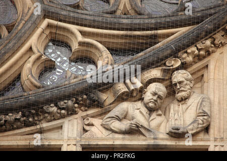 Ritratti di architetti ceca Kamil Hilbert (L) e Josef beffardo (R) raffigurato in bassorilievo da scultore ceco Vojtěch Sucharda (1934) posto sotto il rosone sulla facciata principale di San Vito' cattedrale nel Castello di Praga a Praga, Repubblica Ceca. Foto Stock