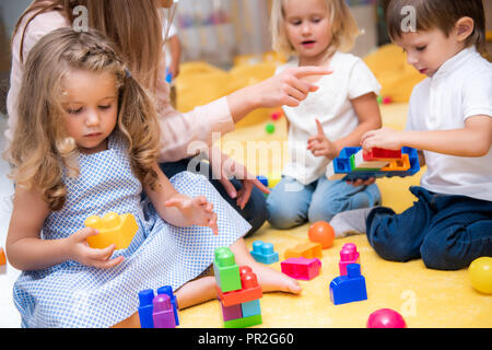 Immagine ritagliata di educatore puntando su qualcosa per i bambini giocando con il costruttore a kindergarten Foto Stock