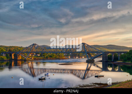 Un ponte che attraversa una baia in Scozia con la riflessione in acqua ferma e accenni del tramonto nel cielo Foto Stock
