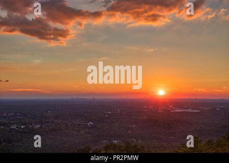Bel colore arancione, rosso, rosa, giallo tramonto con le nuvole e un cielo blu guardando fuori sopra gli alberi verso Atlanta, GA da Stone Mountain Foto Stock