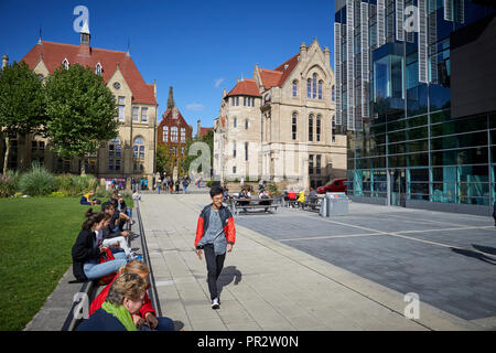 Gli studenti rilassante sull'erba parchi intorno a Manchester Oxford Road Alan Gilbert Learning Commons e Whitworth Hall, Christie's Bistro net-gotico buil Foto Stock