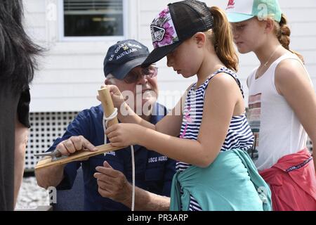 Un membro della Guardia Costiera della flottiglia ausiliari 12-06 insegna ai bambini come legare nodi durante un evento open house alla Stazione della Guardia Costiera Chincoteague, Virginia, luglio 25, 2017. L'unità del personale e degli organi ausiliari ha invitato il pubblico a tour alla stazione Giardini e barche per imparare circa la guardia costiera locale e globale di missioni. Foto Stock