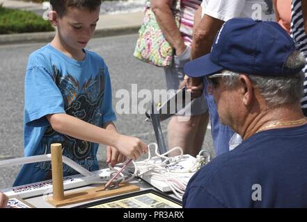 Un membro della Guardia Costiera della flottiglia ausiliari 12-06 insegna ai bambini come legare nodi durante un evento open house alla Stazione della Guardia Costiera Chincoteague, Virginia, luglio 25, 2017. L'unità del personale e degli organi ausiliari ha invitato il pubblico a tour alla stazione Giardini e barche per imparare circa la guardia costiera locale e globale di missioni. Foto Stock