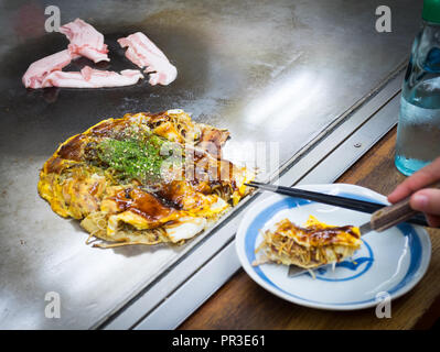 Hiroshima-style okonomiyaki con cavolo, udon noodles, calamari e pancetta e carne di manzo sul grill caldo a Okonomimura a Hiroshima, Giappone. Foto Stock