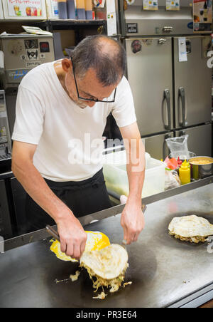 Uno chef che rende lo stile di Hiroshima okonomiyaki a Okonomimura a Hiroshima, Giappone. Foto Stock