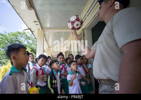 Stati Uniti Air Force Senior Airman Andrew James, 145Ingegnere Civile Squadron ingegnere elettrico, incanta gli studenti di Phan Dinh Phung Scuola primaria come egli gira un pallone da calcio su un dito durante il pacifico Angelo, (PAC ANGEL) 18-2 in Tam Phuoc comune, l'unità PHU Ninh district, Vietnam, Sett. 11, 2018. Durante il PAC ANGELO 18-2 ingegneri civili ha lavorato sulle riparazioni, ristrutturazioni e gli aggiornamenti alle attuali otto medico rurale e delle strutture scolastiche. PAC Angel è un multilaterale di assistenza umanitaria civile e militare, di impegno che migliora di strutture militari di partenariati nell'Indo-Pacifico fornendo anche medica Foto Stock