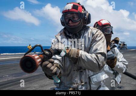 Mare delle Filippine (17 settembre 2018) marinai del crash e equipaggio di soccorso contro un aereo simulato il fuoco come parte di una massa casualty drill sul ponte di volo della Marina è distribuita portaerei USS Ronald Reagan (CVN 76) durante la Valiant scudo 2018. La biennale, SOLO NEGLI STATI UNITI, campo-esercizio di formazione si concentra sull'integrazione di formazione congiunta tra Stati Uniti Navy, Air Force e Marine Corps. Questo è il settimo esercizio nel Valiant scudo serie che ha avuto inizio nel 2006. Foto Stock