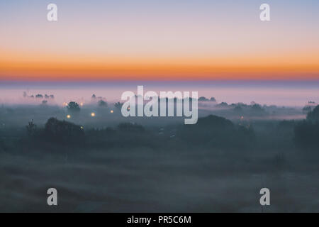 Alba nella nebbia in un piccolo villaggio in mezzo a una foresta di piccole dimensioni. Vista superiore Foto Stock