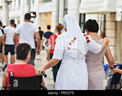 Christian nun camminare per la strada e aiutare la donna in sedia a rotelle Foto Stock