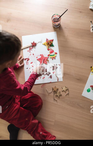 Ragazzo giovane effettuare decorazioni seduta sul pavimento della pittura o fare artigianato, vista dall'alto. Foto Stock