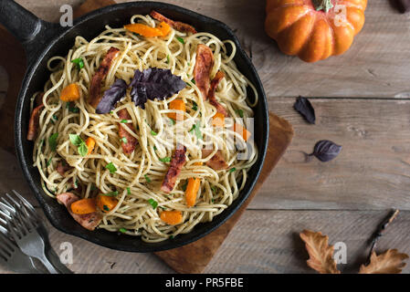 In autunno la pasta con zucca e pancetta in ghisa pan. Spaghetti fatti in casa di zucca sulla pasta di legno, copia dello spazio. Autunno alimento stagionale. Foto Stock