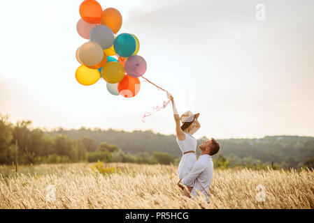 Amore giovane con palloncini abbraccia in un campo di segale. Donna graziosa sul prato estivo Foto Stock