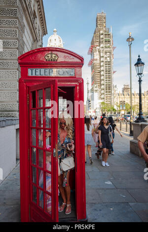 Londra, Inghilterra - Agosto 4, 2018: Donna e bambino esce da un tradizionale rosso cabina telefonica di Londra e Big Ben Clock Tower in manutenzione nel Foto Stock