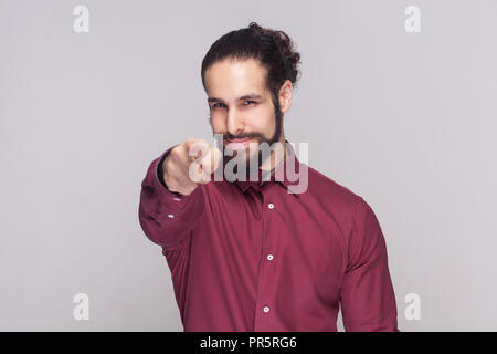 Ehi voi. Ritratto di uomo bello con scuri raccolti i capelli lunghi e la barba in maglietta rossa in piedi, guardando e puntamento in telecamera con gravi faccia ind. Foto Stock