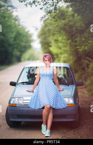 Retrò giovane donna seduta sul cofano delle auto retrò Foto Stock