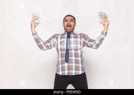 Impazzire con successo!ricco bello uomo barbuto in variopinti camicia a scacchi con cravatta blu in piedi, mantenendo la ventola del contante e celebrazione con open mout Foto Stock