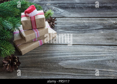 Composizione di natale di coni di pino, abete rami e pila di confezioni regalo con Santa della PAC sullo sfondo della vecchia non verniciata di tavole di legno; con c Foto Stock