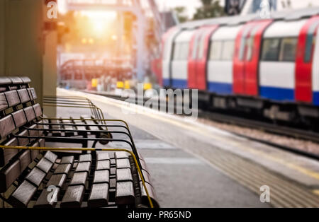 Svuotare panca in legno sulla piattaforma e si avvicina al treno di superficie in background, London, Regno Unito Foto Stock