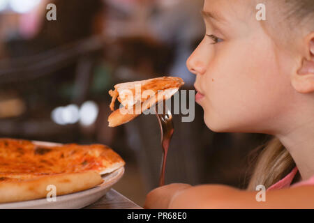 Una piccola ragazza bella di mangiare la pizza con una forchetta in un  ristorante Foto stock - Alamy