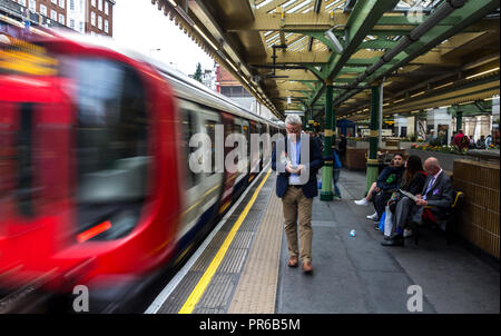 Un occupato il vecchio uomo in attesa del suo treno di arrivare in modo che egli possa raggiungere il posto di lavoro a Londra. Foto Stock