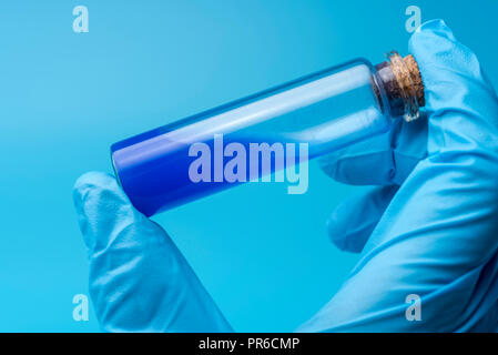 Close-up di tubo di vetro con fluido blu in mano dello scienziato durante il test medici. Una mano tiene un pallone di liquido di colore blu. Foto Stock