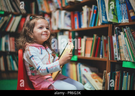 Ragazza carina la lettura di libro in biblioteca. Foto Stock