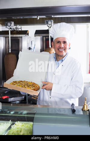 Uomo maturo cuoco indossando uniforme che serve pizza fresca al cliente nel ristorante Foto Stock