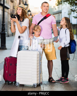 Allegro sorridente famiglia turistiche usando la mappa e prendendo foto della città passeggiando con telecamera e telefono Foto Stock