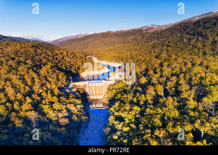 Massiccio Guthega calcestruzzo diga sul fiume nevoso blocca il flusso e la formazione di acqua fresca serbatoio e la generazione di energia rinnovabile nelle montagne innevate tra Foto Stock