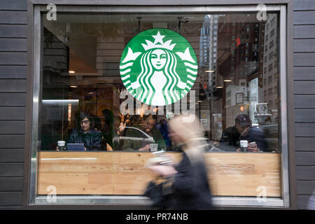 Una donna cammina davanti a uno Starbucks sulla Fifth Avenue a New York City in un nuvoloso mattina di settembre. Foto Stock