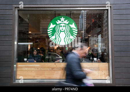 Un imprenditore controlla il telefono cellulare mentre si cammina passato uno Starbucks sulla Fifth Avenue a New York City in un nuvoloso mattina di settembre. Foto Stock