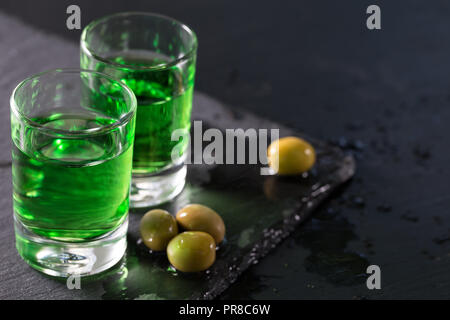 Due bicchieri di forte assenzio e olive verdi su sfondo nero Foto Stock