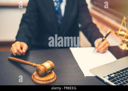 Avvocato tenendo la penna con la scrittura su carta bianca e martello di legno giudice in aula, avvocato giudice nozione Foto Stock