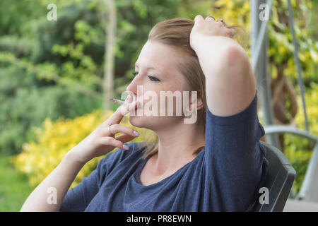 Vista laterale di soggetti di razza caucasica capelli lunghi bruna giovane donna Sigaretta fumare all'esterno. Foto Stock